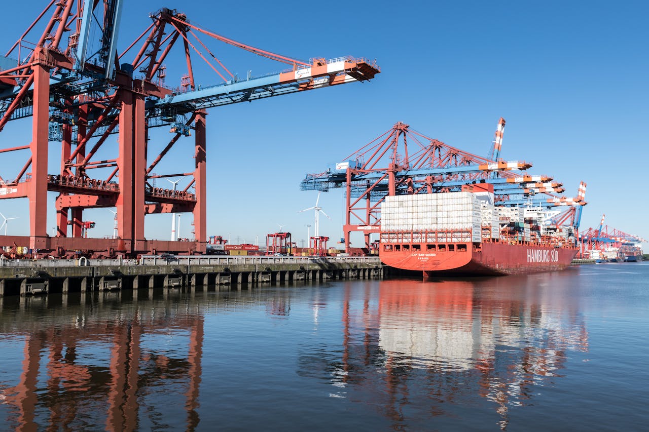 Container ship at Hamburg port with cranes on a clear day, showcasing industrial operations.